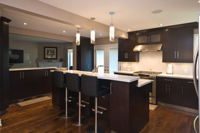 Large minimalist l-shaped medium tone wood floor open concept kitchen photo in Toronto with an undermount sink, flat-panel cabinets, dark wood cabinets, quartz countertops, white backsplash, stone slab backsplash, stainless steel appliances and an island
