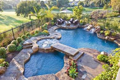 Design ideas for a large tropical backyard custom-shaped pool in Orange County with a hot tub and natural stone pavers.
