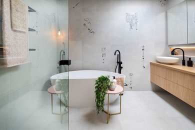 Design ideas for a mid-sized modern 3/4 bathroom in Melbourne with furniture-like cabinets, medium wood cabinets, a freestanding tub, a curbless shower, a wall-mount toilet, gray tile, porcelain tile, grey walls, porcelain floors, a vessel sink, wood benchtops, grey floor and a hinged shower door.
