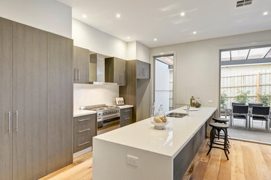 Design ideas for a mid-sized contemporary galley kitchen in Melbourne with a double-bowl sink, white splashback, stainless steel appliances, light hardwood floors, with island and white benchtop.