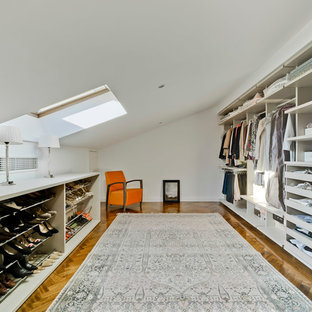 Imagen de vestidor de mujer, actual, grande, con armarios abiertos, puertas de armario blancas y suelo de madera en tonos medios
