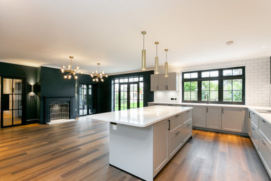 Design ideas for a grey and teal l-shaped kitchen/diner in Kent with a submerged sink, raised-panel cabinets, grey cabinets, quartz worktops, white splashback, porcelain splashback, black appliances, vinyl flooring, an island, brown floors, white worktops and a chimney breast.