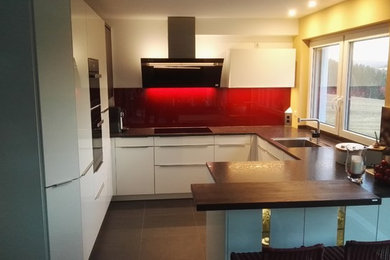 Offene Moderne Küche in U-Form mit weißen Schränken, Granit-Arbeitsplatte, Küchenrückwand in Rot, Küchengeräten aus Edelstahl und Halbinsel in Stuttgart