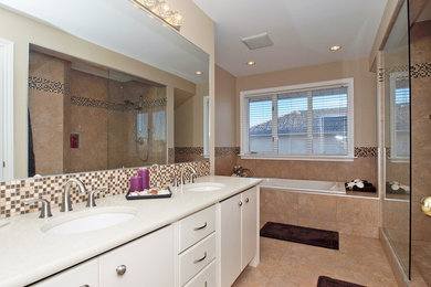This is an example of a large contemporary master bathroom in Calgary with flat-panel cabinets, white cabinets, a drop-in tub, a corner shower, beige tile, ceramic tile, beige walls, ceramic floors, an undermount sink and solid surface benchtops.