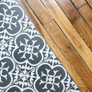 Новые идеи обустройства дома: маленькая п-образная кухня-гостиная в стиле модернизм с накладной раковиной, плоскими фасадами, белыми фасадами, столешницей из акрилового камня, белым фартуком, фартуком из плитки кабанчик, черной техникой, полом из цементной плитки, серым полом и черной столешницей без острова