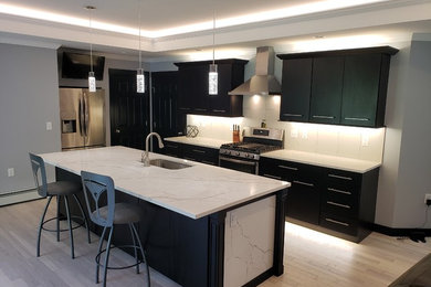 Open concept kitchen - modern galley light wood floor and white floor open concept kitchen idea in Other with an undermount sink, flat-panel cabinets, black cabinets, quartzite countertops, white backsplash, stainless steel appliances, an island and white countertops