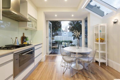 This is an example of a contemporary eat-in kitchen in Sydney with white cabinets, limestone benchtops, white splashback, ceramic splashback, stainless steel appliances, light hardwood floors and brown floor.