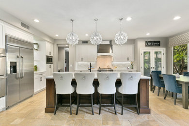 Open concept kitchen - huge transitional u-shaped travertine floor and beige floor open concept kitchen idea in Orange County with a single-bowl sink, shaker cabinets, white cabinets, quartz countertops, multicolored backsplash, stone tile backsplash, stainless steel appliances, an island and white countertops