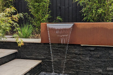 Photo of a small contemporary back partial sun garden for autumn in Cheshire with a water feature, natural stone paving and a wood fence.