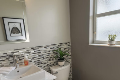 Design ideas for a small transitional powder room in Miami with flat-panel cabinets, grey cabinets, a one-piece toilet, gray tile, matchstick tile, grey walls, porcelain floors, granite benchtops, brown floor, white benchtops and a freestanding vanity.