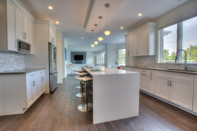 Inspiration for a large contemporary l-shaped porcelain tile and black floor open concept kitchen remodel in Bridgeport with an undermount sink, shaker cabinets, white cabinets, quartz countertops, white backsplash, glass tile backsplash, stainless steel appliances and an island