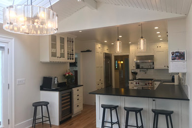 Example of a mid-sized classic u-shaped medium tone wood floor enclosed kitchen design in Seattle with an undermount sink, shaker cabinets, white cabinets, granite countertops, white backsplash, ceramic backsplash, stainless steel appliances, a peninsula and black countertops