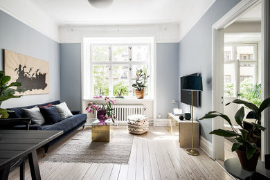 Design ideas for a mid-sized scandinavian open concept living room in Stockholm with blue walls, light hardwood floors and a wall-mounted tv.
