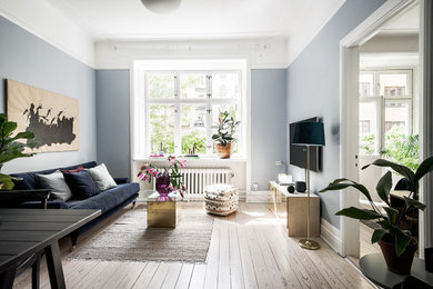 Foto på ett mellanstort minimalistiskt allrum med öppen planlösning, med blå väggar, ljust trägolv och en väggmonterad TV