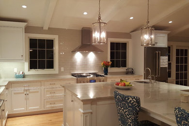 Photo of a mid-sized traditional l-shaped open plan kitchen in Philadelphia with a farmhouse sink, beaded inset cabinets, white cabinets, quartzite benchtops, grey splashback, porcelain splashback, stainless steel appliances, light hardwood floors and with island.