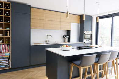 Medium sized modern galley kitchen/diner in London with flat-panel cabinets, blue cabinets, quartz worktops, stainless steel appliances, light hardwood flooring, an island and grey worktops.