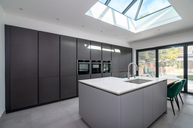 Photo of an expansive modern grey and black kitchen/diner in London with flat-panel cabinets, grey cabinets, quartz worktops, engineered quartz splashback, integrated appliances, porcelain flooring, an island, grey floors and white worktops.