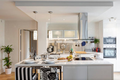 Large contemporary l-shaped eat-in kitchen in Paris with an undermount sink, beaded inset cabinets, white cabinets, laminate benchtops, grey splashback, metal splashback, black appliances, light hardwood floors, with island and brown floor.