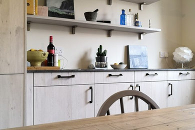 Photo of a mid-sized traditional l-shaped eat-in kitchen in Edinburgh with a drop-in sink, flat-panel cabinets, light wood cabinets, laminate benchtops, grey splashback, glass sheet splashback, stainless steel appliances, vinyl floors and no island.