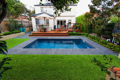 Modelo de piscina moderna pequeña rectangular en patio trasero con adoquines de piedra natural