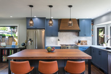 This is an example of a mid-sized beach style l-shaped open plan kitchen in Vancouver with an undermount sink, shaker cabinets, blue cabinets, white splashback, ceramic splashback, stainless steel appliances, with island, brown floor, dark hardwood floors and white benchtop.
