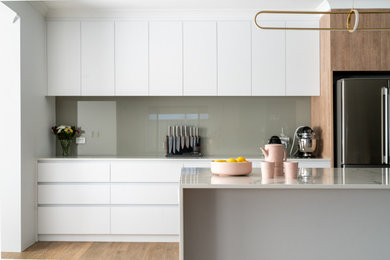 Design ideas for a mid-sized contemporary galley eat-in kitchen in Perth with a double-bowl sink, flat-panel cabinets, light wood cabinets, solid surface benchtops, metallic splashback, glass sheet splashback, stainless steel appliances, ceramic floors, with island, brown floor and white benchtop.