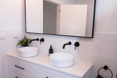 This is an example of a transitional bathroom in Melbourne with shaker cabinets, white cabinets, a freestanding tub, an open shower, white tile, a vessel sink, engineered quartz benchtops and grey floor.