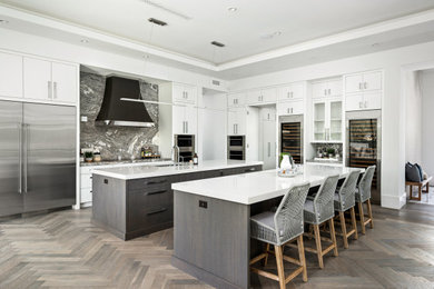 Example of a trendy medium tone wood floor and gray floor kitchen design in Phoenix with flat-panel cabinets, white cabinets, gray backsplash, marble backsplash, stainless steel appliances, two islands and white countertops