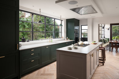 Photo of a transitional galley open plan kitchen in Kent with a triple-bowl sink, shaker cabinets, green cabinets, black appliances, light hardwood floors and with island.