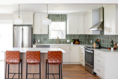 Inspiration for a 1960s l-shaped medium tone wood floor and brown floor kitchen remodel in Boise with green backsplash, stainless steel appliances, white countertops, an undermount sink, shaker cabinets, white cabinets and an island