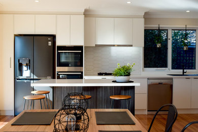 Inspiration for a mid-sized contemporary l-shaped open plan kitchen in Melbourne with a double-bowl sink, flat-panel cabinets, white cabinets, quartz benchtops, white splashback, stone tile splashback, black appliances, medium hardwood floors, with island, brown floor and white benchtop.