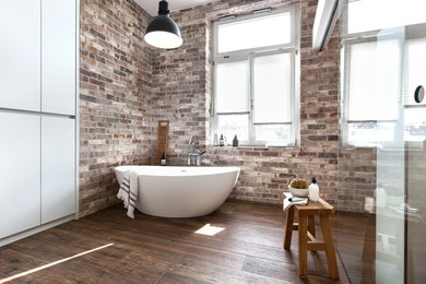 Großes Industrial Badezimmer En Suite mit freistehender Badewanne, braunem Boden, flächenbündigen Schrankfronten, grauen Schränken, Schiebetür-Duschabtrennung, Mineralwerkstoff-Waschtisch, bodengleicher Dusche, Wandtoilette mit Spülkasten, weißer Wandfarbe, Keramikboden, Aufsatzwaschbecken und weißer Waschtischplatte in Frankfurt am Main