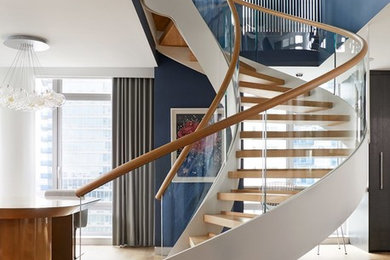 Photo of an expansive contemporary wood curved staircase in New York with glass railing and open risers.