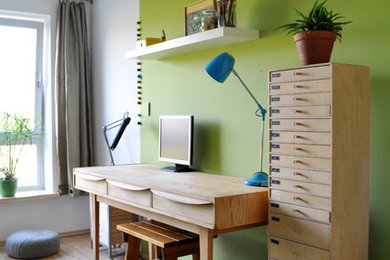 Mittelgroßes Modernes Arbeitszimmer mit Arbeitsplatz, grüner Wandfarbe, braunem Holzboden, freistehendem Schreibtisch und braunem Boden in Berlin