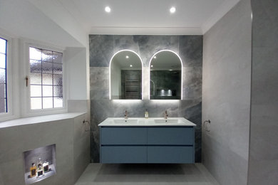 This is an example of a large contemporary ensuite bathroom in Sussex with blue cabinets, beige tiles, porcelain tiles, blue walls, porcelain flooring, solid surface worktops, beige floors, white worktops, double sinks and a floating vanity unit.