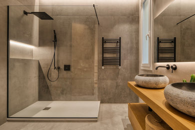 Modern inredning av ett badrum, med svarta skåp, grå kakel, ett fristående handfat och träbänkskiva