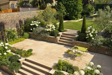 Large contemporary back formal full sun garden wall for summer in London with a raised bed and natural stone paving.
