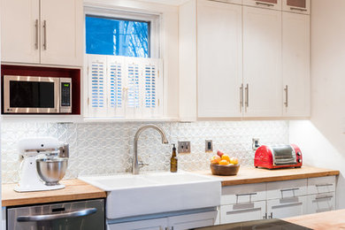 Example of a small galley dark wood floor and black floor enclosed kitchen design in DC Metro with a farmhouse sink, shaker cabinets, white cabinets, wood countertops, metallic backsplash, metal backsplash, stainless steel appliances, an island and multicolored countertops