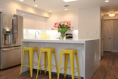 Example of a large trendy l-shaped medium tone wood floor and brown floor kitchen design in New York with an integrated sink, flat-panel cabinets, white cabinets, quartz countertops, white backsplash, glass tile backsplash, stainless steel appliances and an island