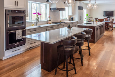 Large country galley light wood floor, brown floor and exposed beam eat-in kitchen photo in Other with an undermount sink, flat-panel cabinets, medium tone wood cabinets, quartz countertops, white backsplash, subway tile backsplash, black appliances, two islands and white countertops
