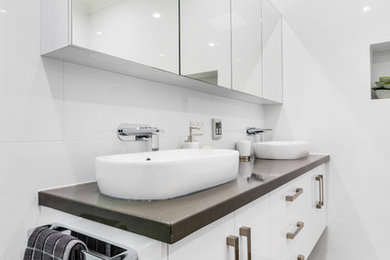 Large modern master wet room bathroom in Adelaide with shaker cabinets, white cabinets, a freestanding tub, a two-piece toilet, white tile, ceramic tile, white walls, ceramic floors, a vessel sink, granite benchtops, brown floor, a hinged shower door and brown benchtops.