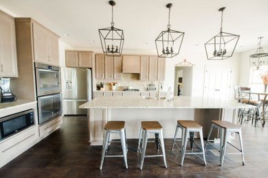 Example of a large transitional single-wall dark wood floor and brown floor open concept kitchen design in Birmingham with an undermount sink, recessed-panel cabinets, light wood cabinets, granite countertops, beige backsplash, stainless steel appliances, an island, stone tile backsplash and white countertops