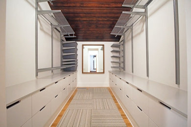 Diseño de armario vestidor unisex minimalista de tamaño medio con armarios con paneles lisos, puertas de armario blancas, suelo de madera clara y madera