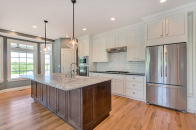 Inspiration for a large farmhouse light wood floor kitchen remodel in San Diego with a farmhouse sink, shaker cabinets, white cabinets, white backsplash, stainless steel appliances and an island