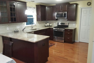 Inspiration for a mid-sized timeless u-shaped medium tone wood floor eat-in kitchen remodel in Raleigh with an undermount sink, dark wood cabinets, granite countertops, beige backsplash, stainless steel appliances, no island and raised-panel cabinets