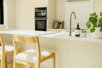 Photo of a large modern galley open plan kitchen in Edinburgh with a built-in sink, shaker cabinets, quartz worktops, white splashback, marble splashback, black appliances, porcelain flooring, an island, beige floors and white worktops.