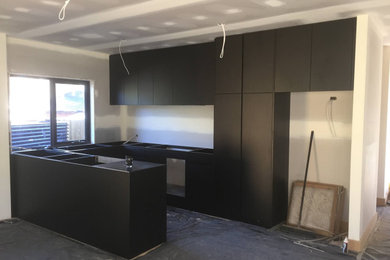 This is an example of a mid-sized contemporary u-shaped eat-in kitchen in Melbourne with a double-bowl sink, flat-panel cabinets, black cabinets, quartz benchtops, white splashback, ceramic splashback, black appliances, vinyl floors, no island and white benchtop.