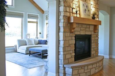 Imagen de salón abierto nórdico de tamaño medio con suelo de madera clara, chimenea de doble cara y marco de chimenea de piedra