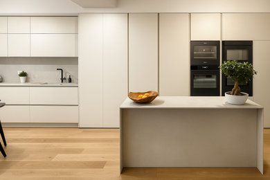 Idee per una grande cucina con lavello integrato, ante lisce, paraspruzzi beige, paraspruzzi in gres porcellanato, elettrodomestici neri, pavimento in legno massello medio, pavimento beige e top beige