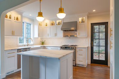 Mid-sized elegant galley medium tone wood floor and brown floor enclosed kitchen photo in Other with a farmhouse sink, shaker cabinets, white cabinets, marble countertops, white backsplash, cement tile backsplash, stainless steel appliances, an island and white countertops
